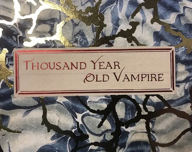La couverture du livre : une &eacute;tiquette de papier coll&eacute;e sur un papier marbr&eacute; bleu et or, o&ugrave; le titre est calligraphi&eacute; en rouge.
